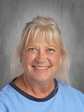 Smiling woman with blonde hair in a blue shirt, set against a gray background.
