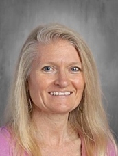 Smiling woman with long blonde hair, wearing a pink top, against a neutral gray background.