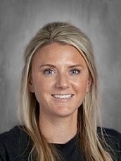 Headshot of a woman with long blonde hair, smiling, wearing a black shirt, against a gray background.